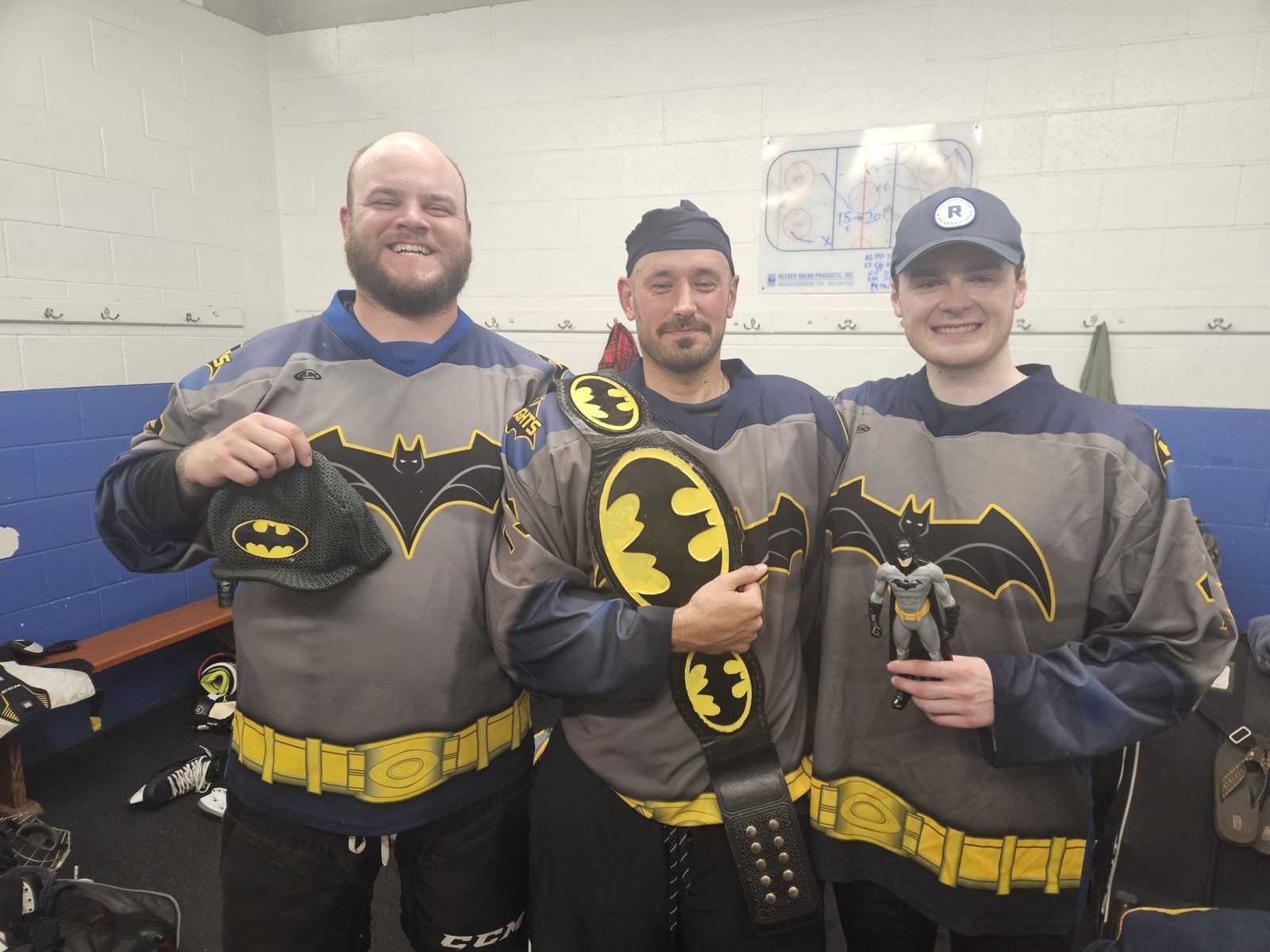 Three Dark Knights players pose in the locker room celebrating with Batman-themed props after the win