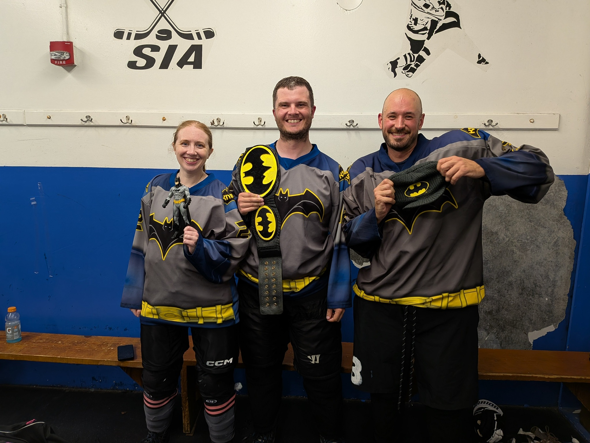 Three Dark Knights players pose in the locker room celebrating with Batman-themed props after the win